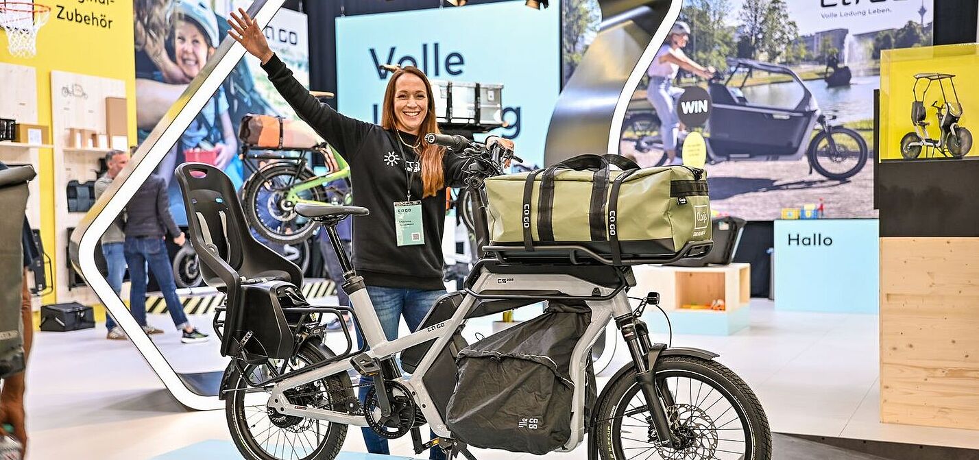 Eurobike Eine Frau steht an einem Messestand und präsentiert ein Lastenrad.